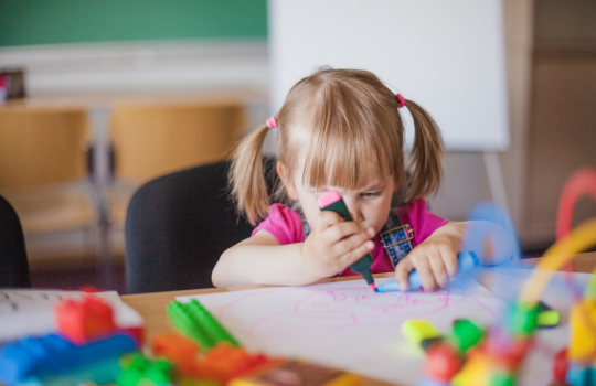 Enfant tenant un feutre rose fluo et dessinant