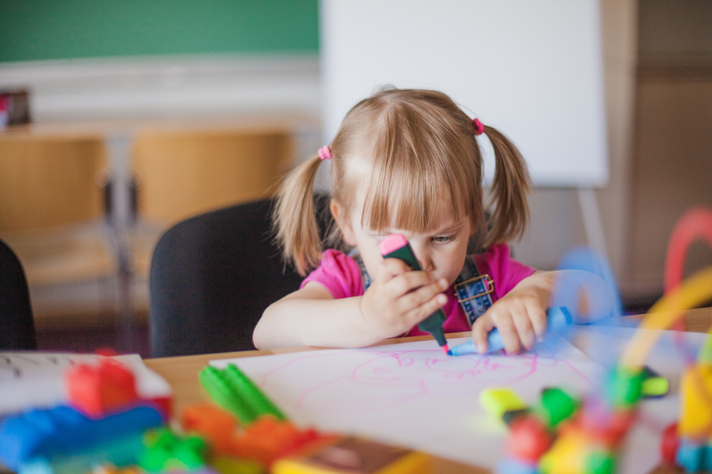 Enfant tenant un feutre rose fluo et dessinant